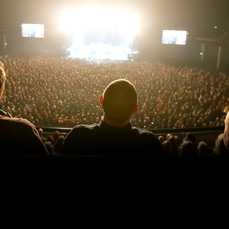 image of the back of a mans head in the audience, facing towards the stage
