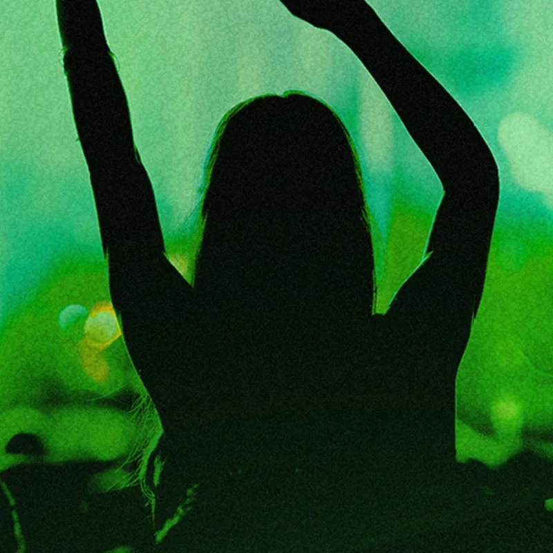 behind shot of woman dancing at a concert in green lighting