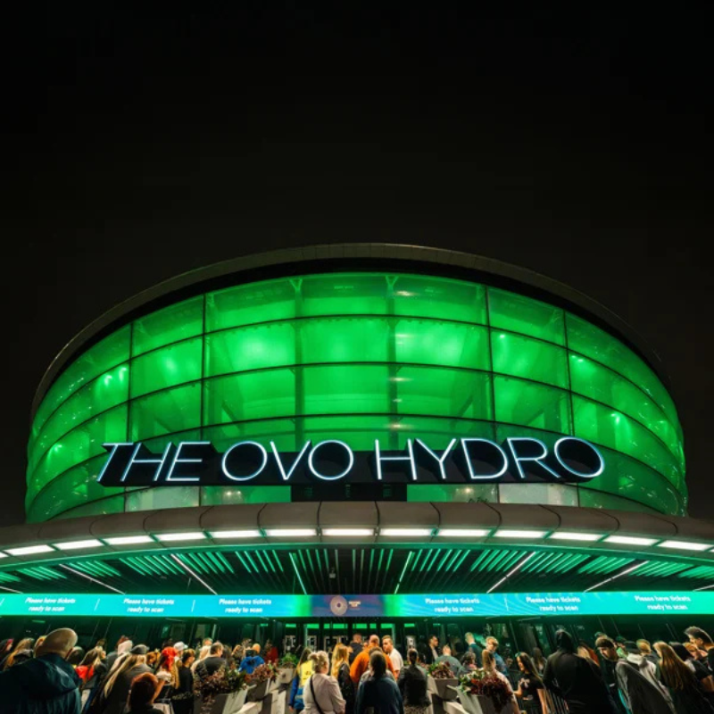 Image of OVO Hydro at night lit up green with people queuing to get inside