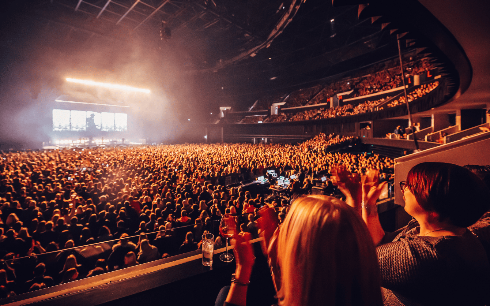 View of the stage and standing crowd from seats. Two women are clapping.
