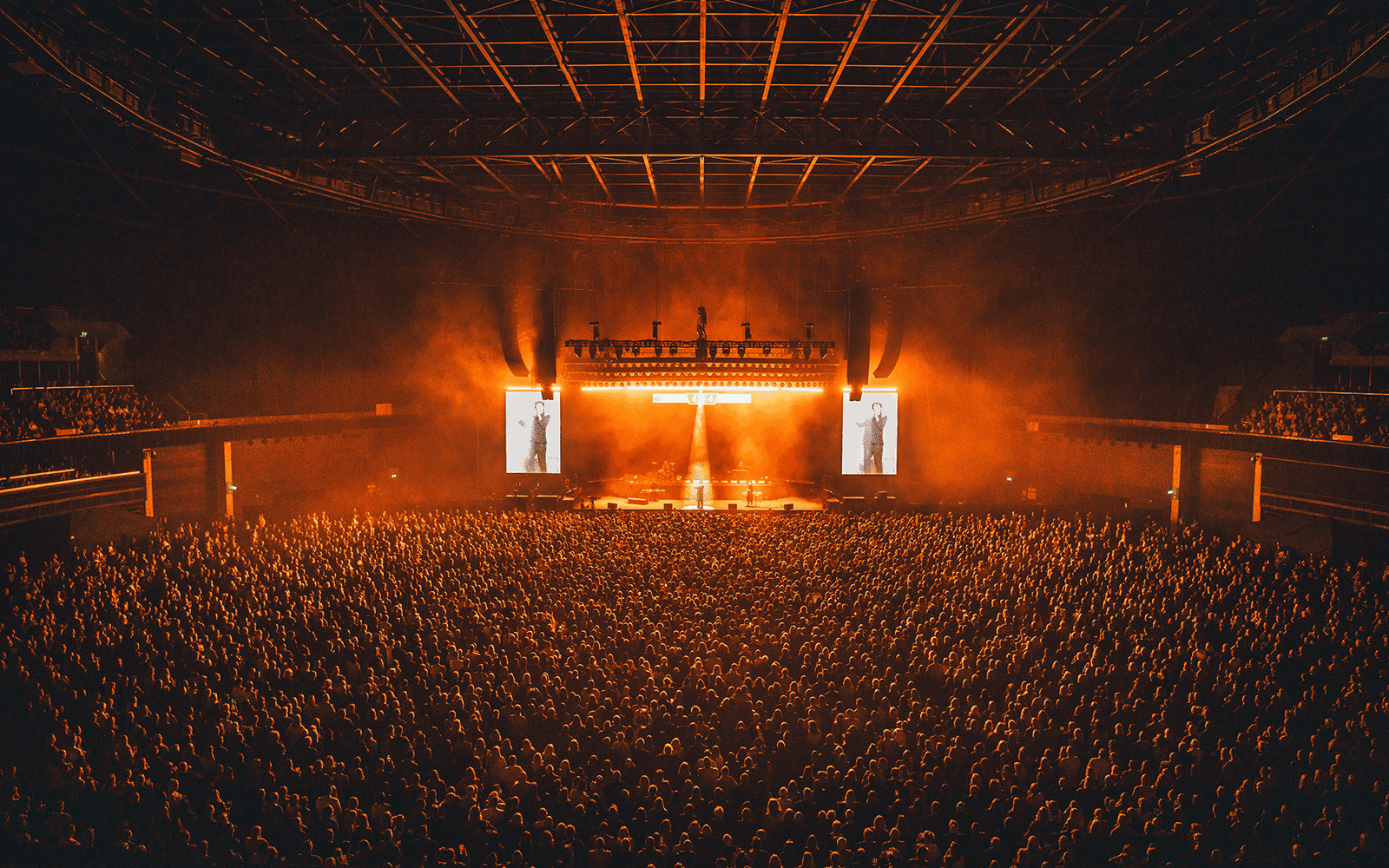 Artist performing on stage at the OVO Hydro, the standing section is full of people and the lighting makes the image look orange. 