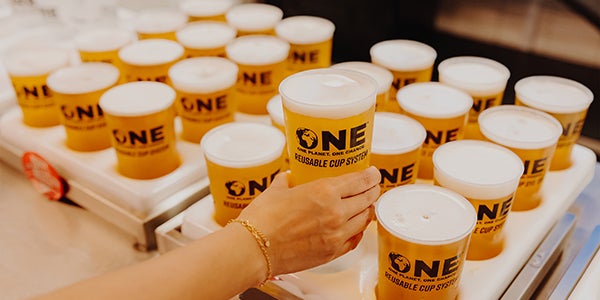 Numerous One Cups filled with beer. Someone is taking one of the cups.