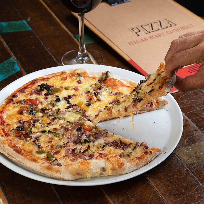 person picking up slice of pizza from full pizza at clydebuilt